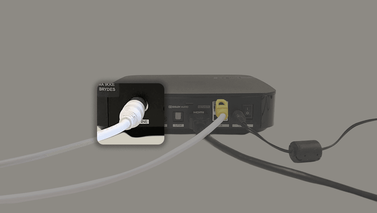 Tv-boks med tilsluttet koaksialkabel og HDMI-kabel samt tænd/sluk-knap på bagsiden.